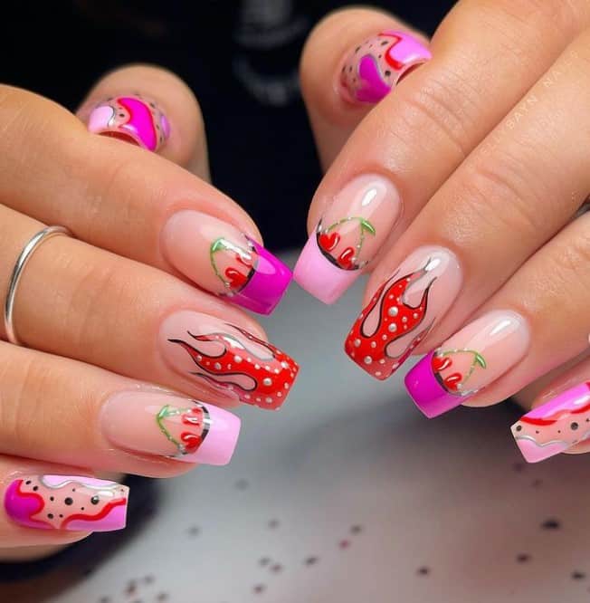 A closeup of a woman's hands with a glossy nude nail polish that has hot cherry and flame nail design theme