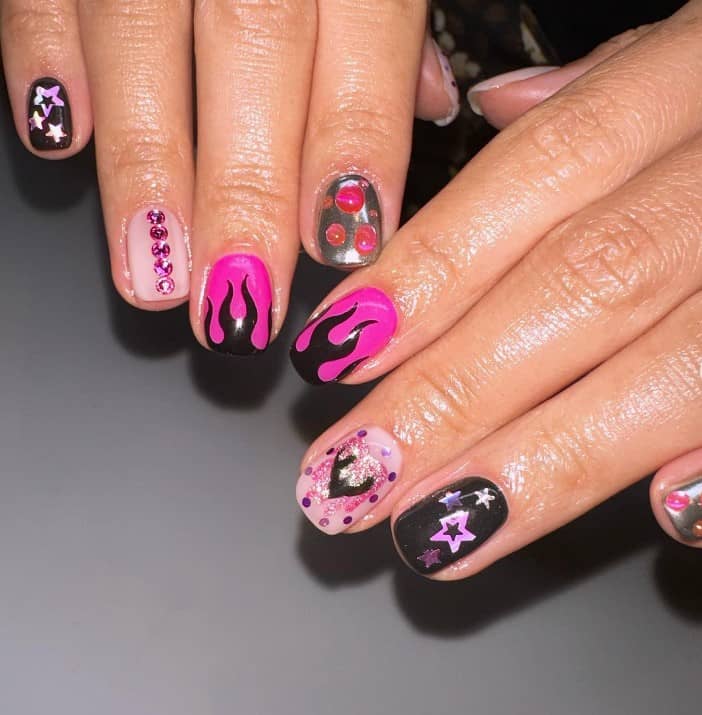 A closeup of a woman's hands with a combination of nude, pink and black nail polish that has pink shiny 3D decor and black flames