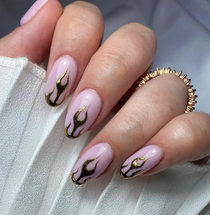 A closeup of a woman's hand with a creamy nude glossy nail polish that has chrome gold flame tips