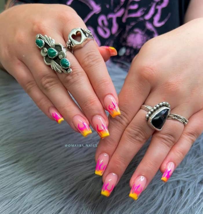 A closeup of a woman's hands with a nude nail polish base that has a neon yellow-tipped pink flame design