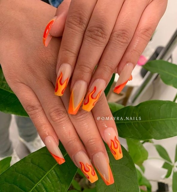 A closeup of a woman's hands with nude nail polish that has orange flame on nail tips