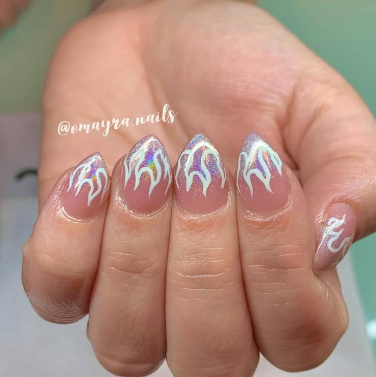 A closeup of a woman's hand with a pink nail polish that has white flame nail designs and silver glitter