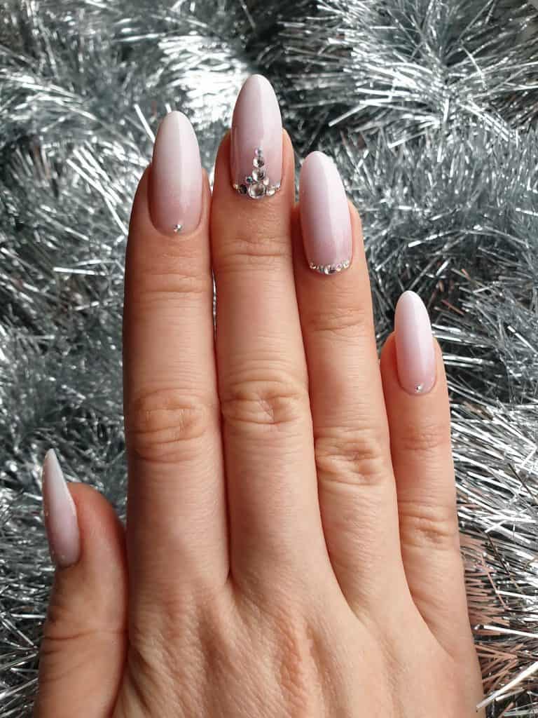 A closeup of a woman's hand with a pale pink nail polish base that has white nail tips and gems nail designs on select nails