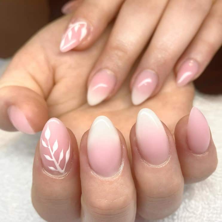 A closeup of a woman's hands with nude nail polish that has white nail tips and plain white flower on select nails 