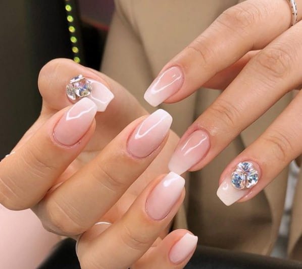 A closeup of a woman's hands with pale pink nail polish and white nail tips that has gems on select nails