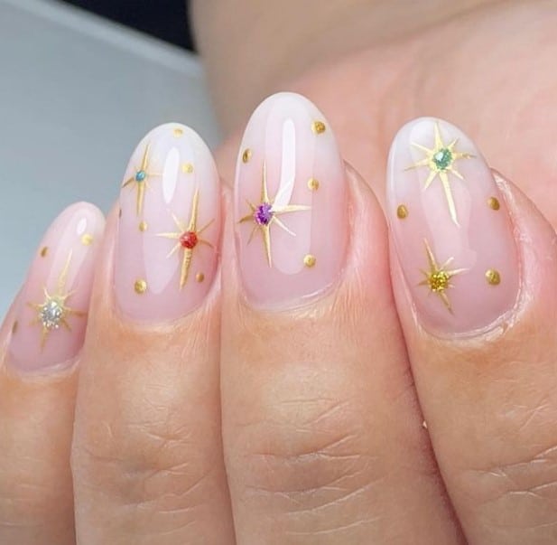 A closeup of a woman's hand with pale pink ombré base that has white nail tips and multicolored evening stars nail designs