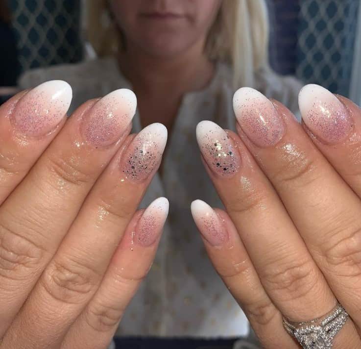 A woman's hands with a nude nail polish base and white nail tips that has Rose gold glitters 