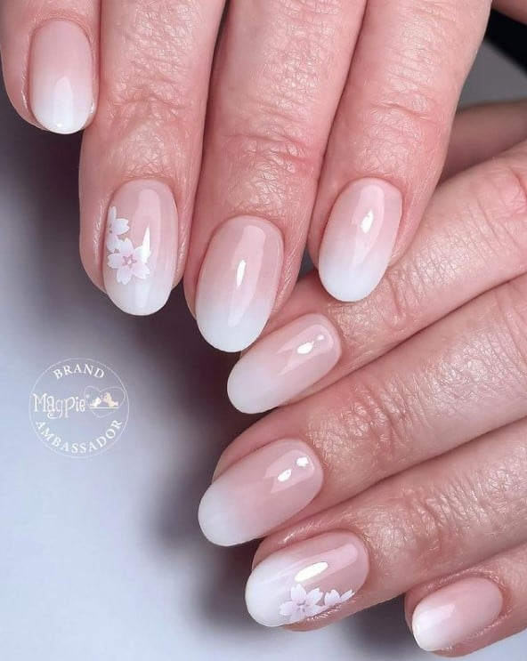 A closeup of a woman's hands with a glossy pale pink nail polish that has white nail tips and cherry blossoms nail designs