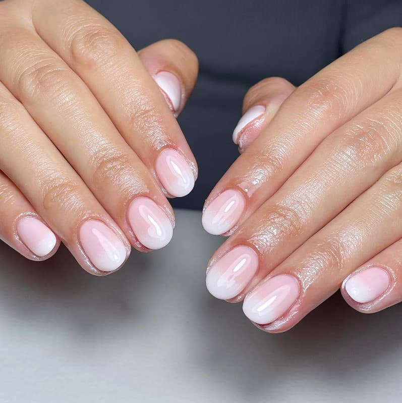 A woman's hands with glossy pale pink nail polish base that has white nail tips 