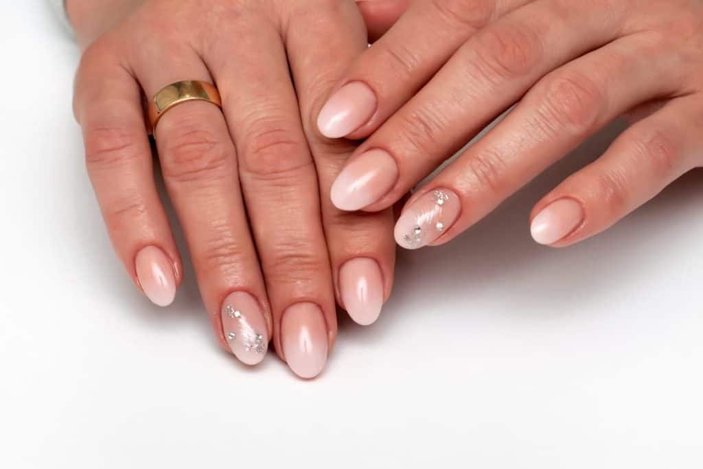 A woman's hands with nude nail polish that has rhinestone accents on only one finger