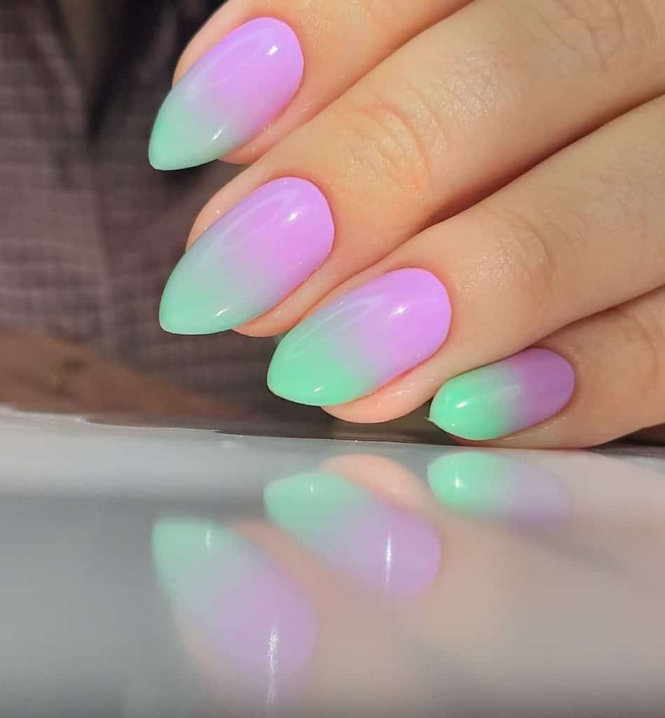 A closeup of a woman's hand with purple nail polish base that has mint green nail tips 