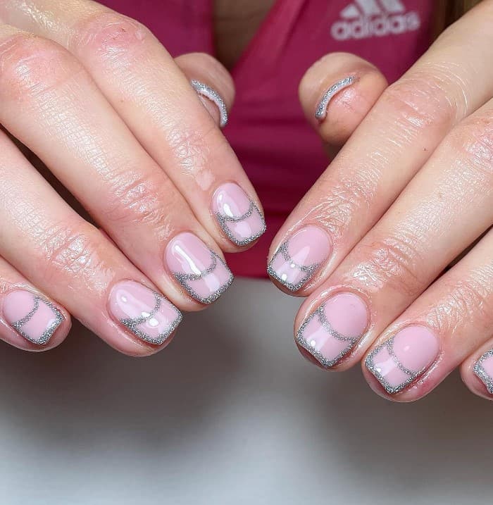 A closeup of a woman's hands with nude nail polish that has silver glitter polish  tips