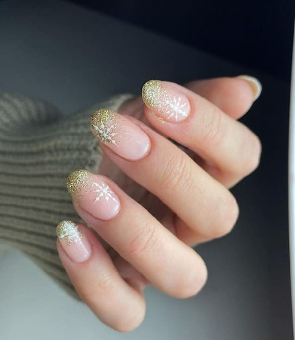 A closeup of a woman's hand with nude nail polish base that has glitter and snowflake decorations 