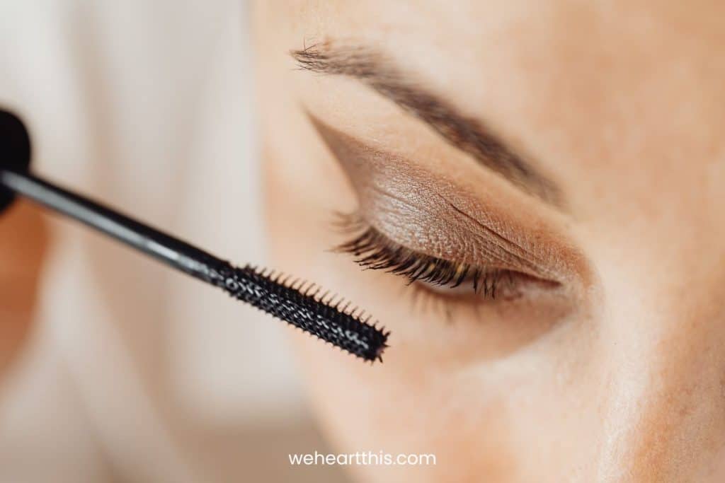 A cropped view of a woman's eye applying mascara to her lashes 