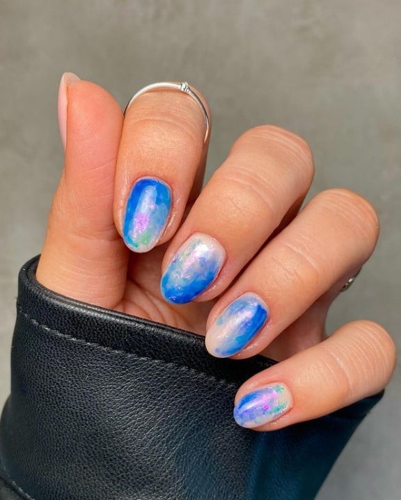 A closeup of a woman's fingernails with a combination of white and blue marble nail polish