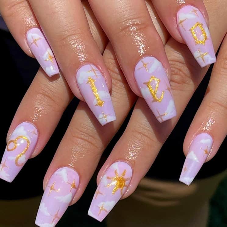 A closeup of a woman's fingernails with baby pink nail polish that has clouds for a touch of white and zodiac symbol in lovely gold glitters