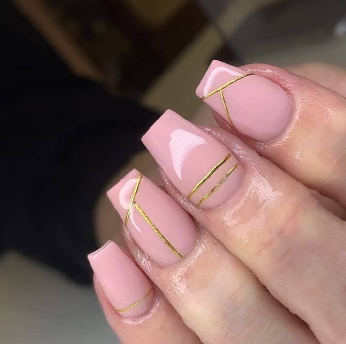 A closeup of a woman's fingernails with pink nail polish that has minimalist lines in gold polish
