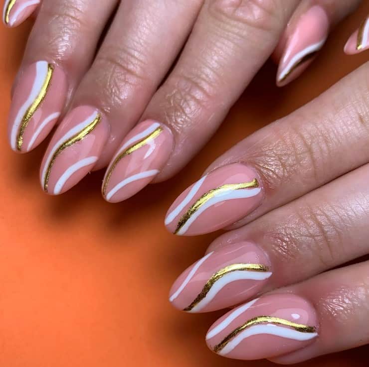 A closeup of a woman's fingernails with glossy pink nail polish that has curves of white and gold