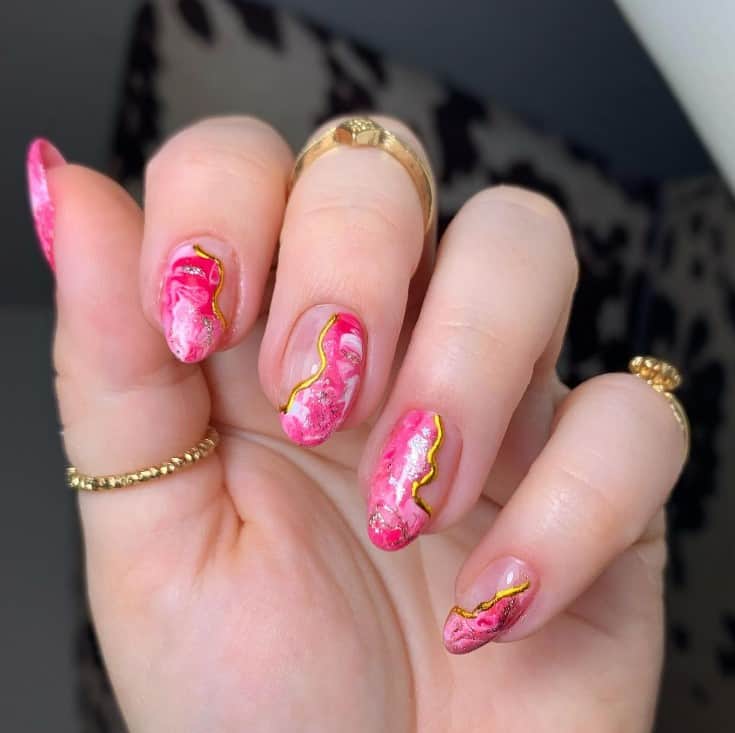 A closeup of a woman's fingernails with a tie-dye inspired pink nail polish that has a wave of gold polish 