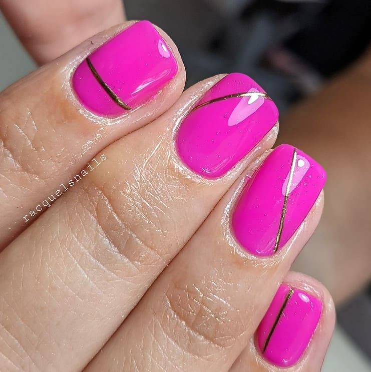 A closeup of a woman's fingernails with a hot pink nail polish that has gold nail designs