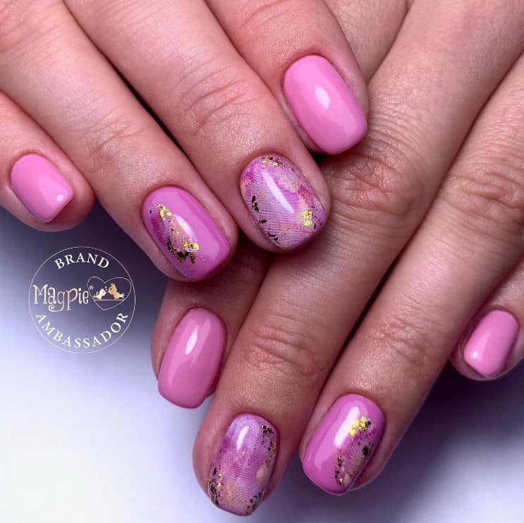 A closeup of a woman's fingernails with pink nail polish that has gold nails design with the magic of nail stamping and gold foil