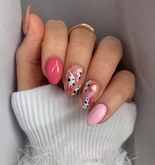 A closeup of a woman's fingernails with light pink with hot pink nail polish that has gold nail designs and black dots