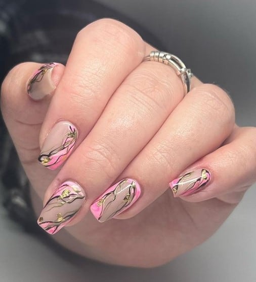 A closeup of a woman's fingernails with pink nail polish base that has streaks of black and add flakes of gold foil