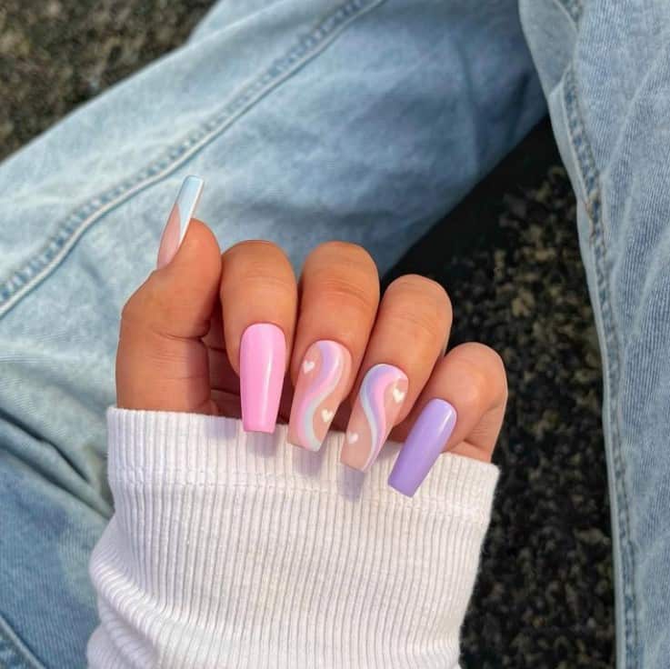 A closeup of a woman's fingernails with a combination of pink and purple nail polish that has pastel-colored curved lines, tips, and hearts nail designs