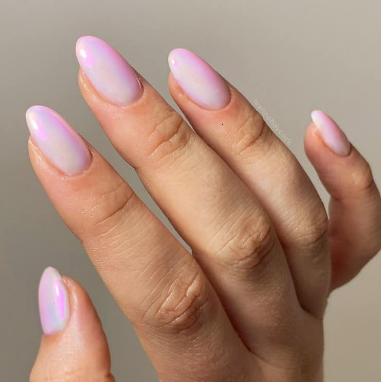 A closeup of a woman's fingernails with a pearly white nail polish base that has holographic pink and purple tones 