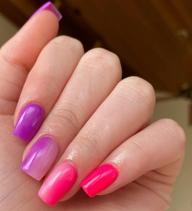 A closeup of a woman's fingernails with ombre pink and purple nail polish 