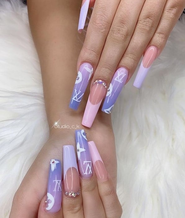A woman's fingernails with a pink and purple acrylic nail polish that has pink and purple French tips, tiny rhinestones and iconic Louis Vuitton symbols