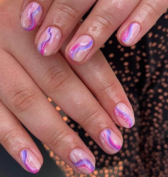 A closeup of a woman's fingernails with a glossy nude nail polish that has thin streaks of pink, purple, and glittery rose gold