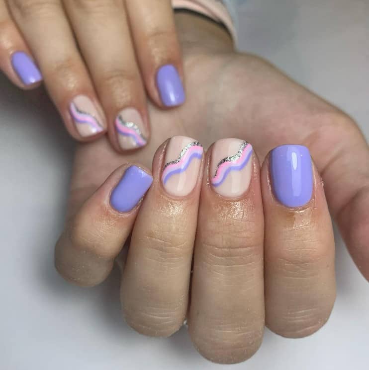 A closeup of a woman's fingernails with a nude and purple nail polish that has squiggles in pink, purple, and glittery silver 