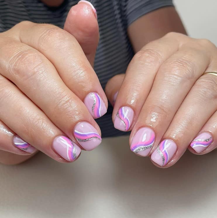 A woman's fingernails with a dusty rose pink nail polish that has thin streaks of pink, purple, white, and glittery silver