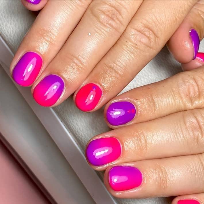 A closeup of a woman's fingernails with pink and purple ombre nail polish that has vertical and horizontal gradient styles and small dots on select nails