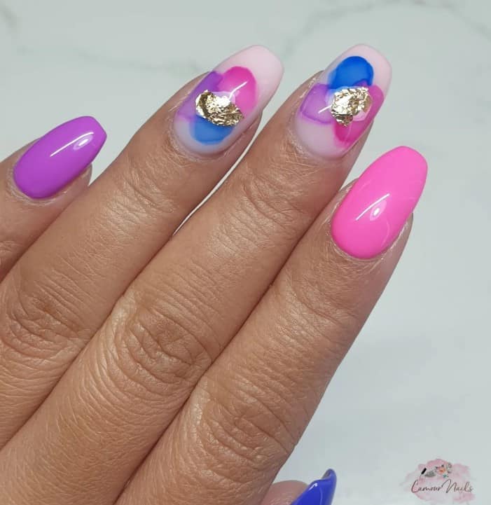 A closeup of a woman's fingernails with a combination of white, pink, light pink, blue, and purple nail polish that has smudges of blue, pink, and purple and a touch of glam from the gold foil