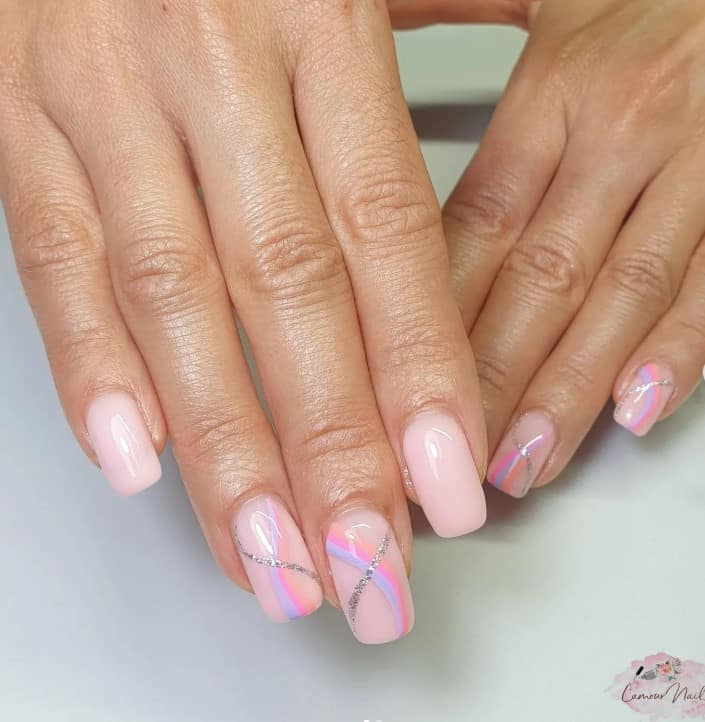 A closeup of a woman's fingernails with a milky pink nail polish base that has pink, purple, and peach streaks, and a lone glittery silver streak