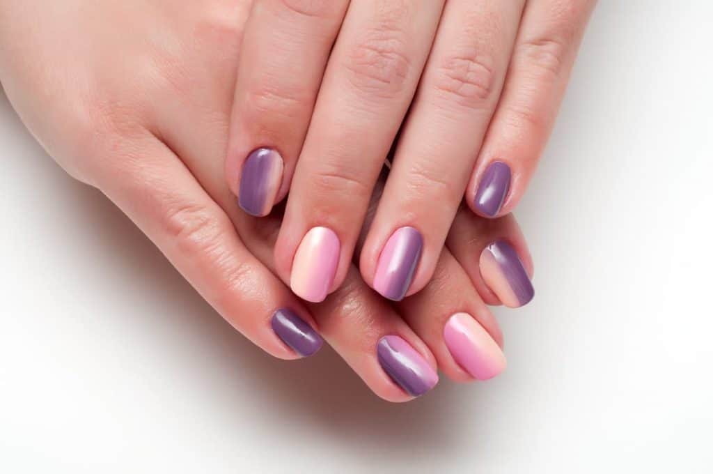 A woman's fingernails with a combination of dark purple and light peach ombre nail polish