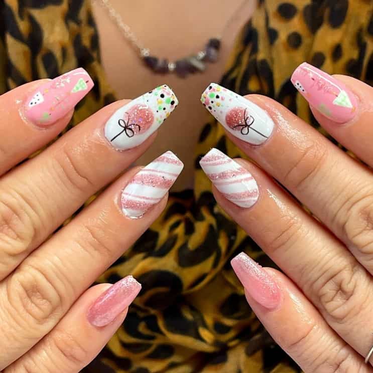 A closeup of a woman's hands with a mix of white and pink nail polish base that has inverted triangles, cute lollipops, polka dots, stripes, and glitter nail designs
