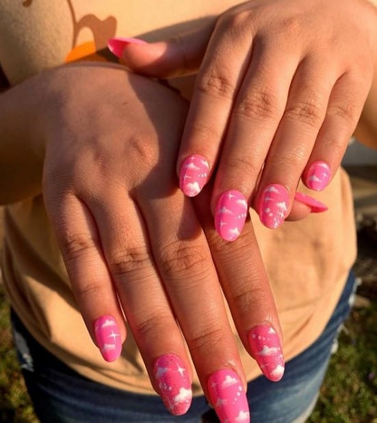 A closeup of a woman's hands with hot-pink-and-white nail polish that has cloud designs 