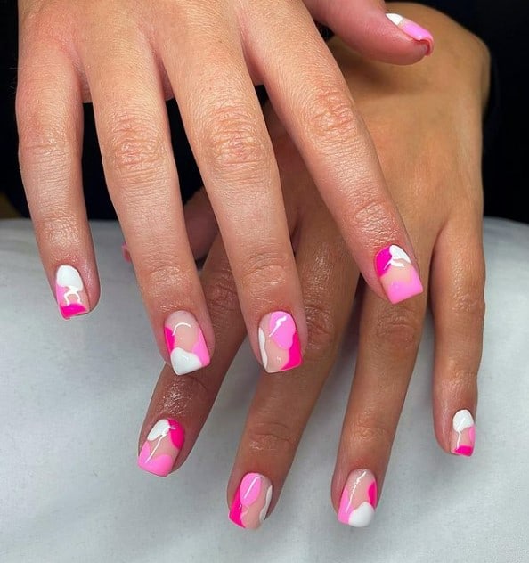 A closeup of a woman's hands with a nude nail polish base that has splatters of light pink, bright pink, and white nail polish