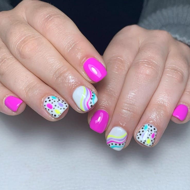 A closeup of a woman's hands with a combination of white and pink nail polish that has candy colors and black dots nail designs
