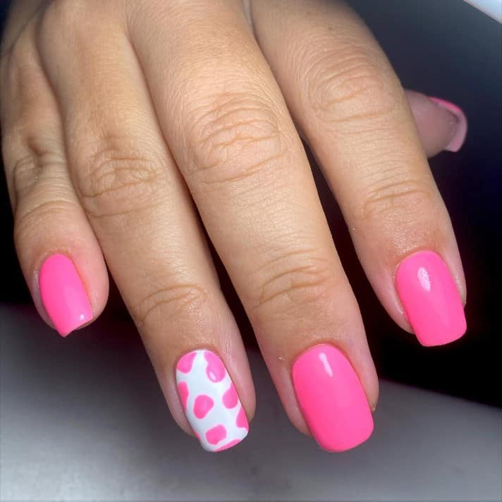 A closeup of a woman's hand with a combination of pink and white nail polish that has pink spots on the white polish