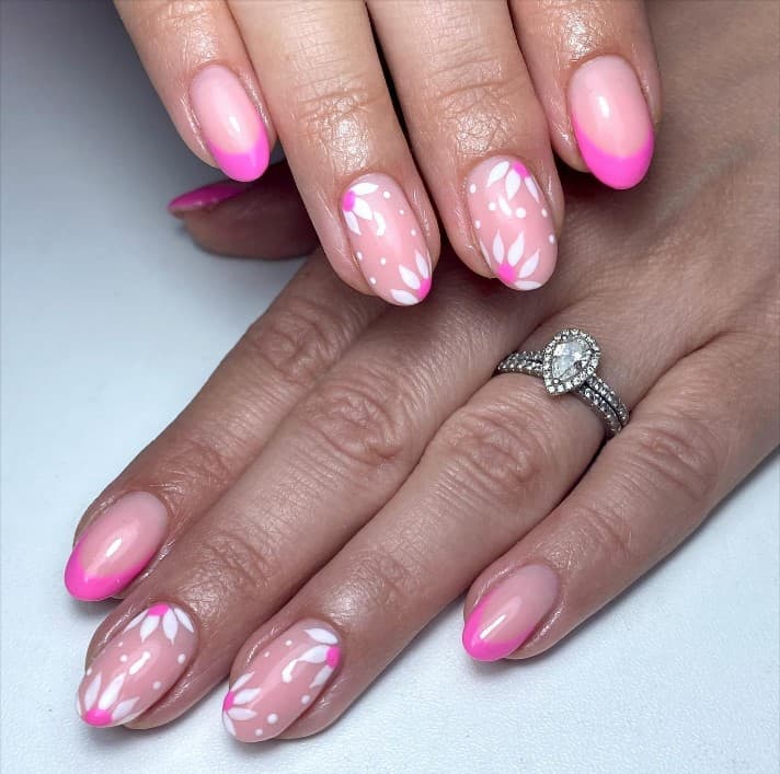 A closeup of a woman's hands with a nude nail polish that has hot pink tips with flower nail art
