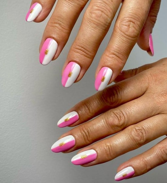 A closeup of a woman's hands with pink and white nail polish that take up half of each nail. It has  a dab of gold glitter polish