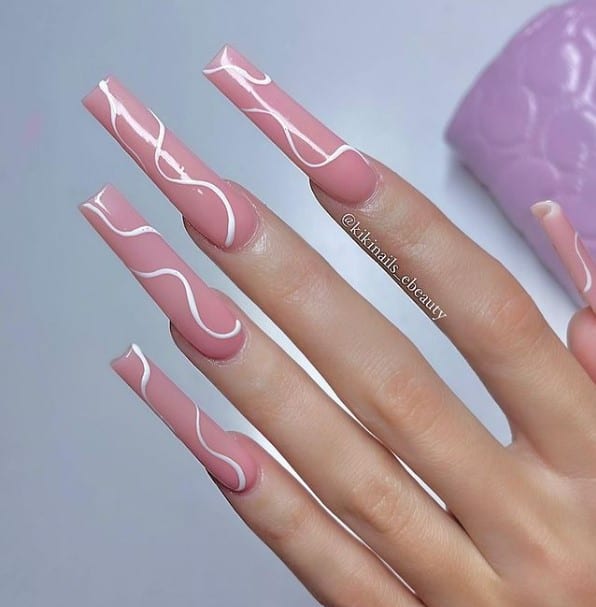A closeup of a woman's hands with a long and pink nail polish that has white curved lines painted on each nail