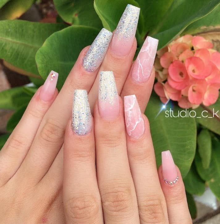 A closeup of a woman's hands with Ombré pink-and-white nails that has glitter and  translucent pink marble nails