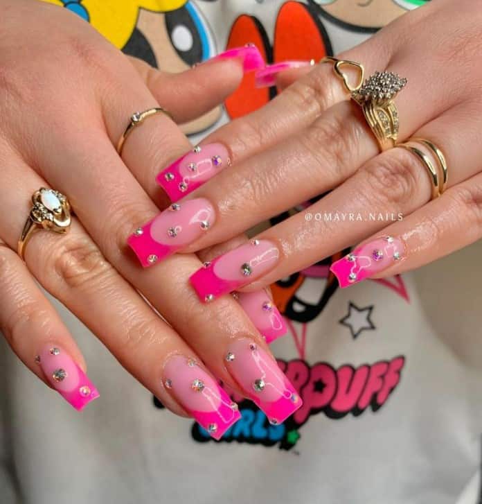 A closeup of a woman's hands with pale pink nail polish base that has hot pink French tip nails and chrome studs