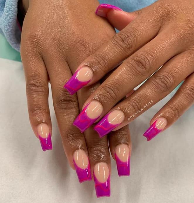 A closeup of a woman's hands with nude nail polish base that has pink streaks on magenta nail tips