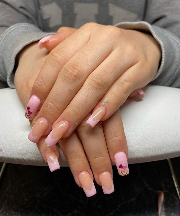 A woman's hands with nude nail polish base that has baby pink-tipped nails and topped with dainty hearts in red, pink, and gold